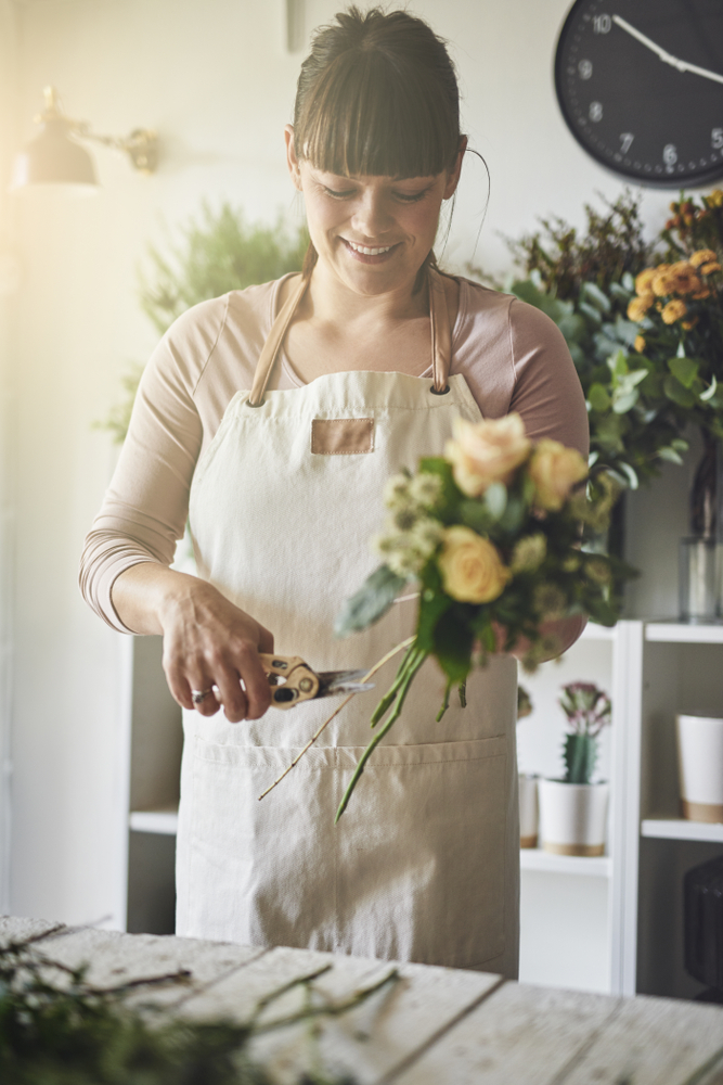 Smiling,Young,Female,Florist,Standing,At,A,Table,In,Her