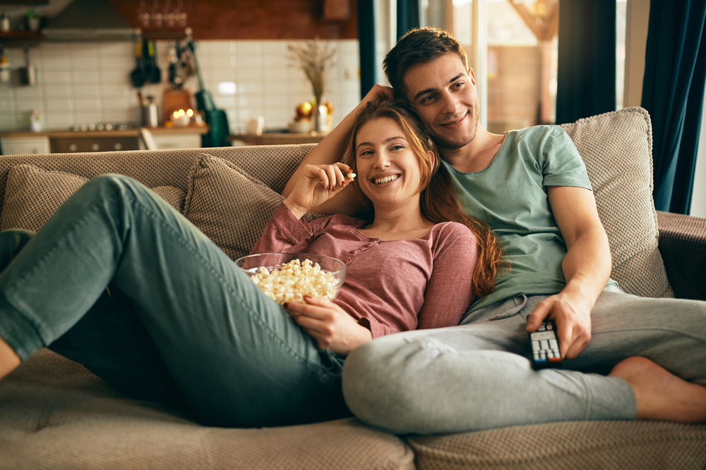 Young,Happy,Couple,Watching,Movie,On,Tv,And,Eating,Popcorn