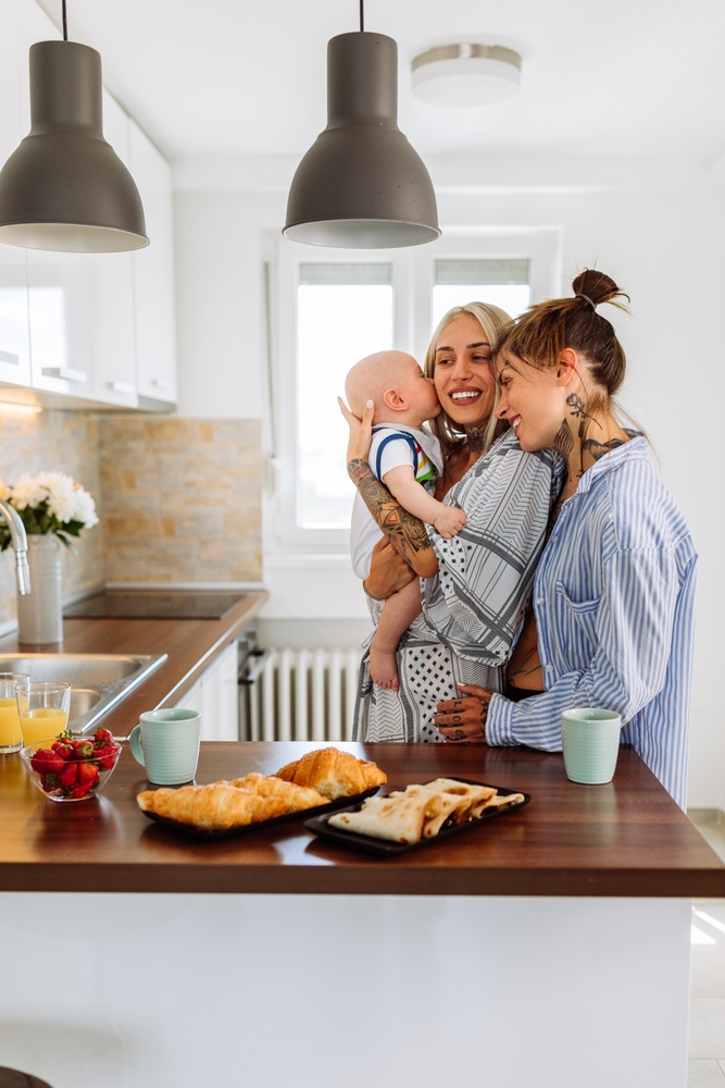 Same,Sex,Couple,Cuddling,With,Their,Baby,Son,In,Their