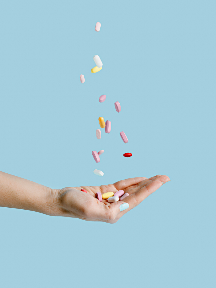Woman's,Hand,With,Falling,Medical,Pills,Isolated,On,Pastel,Blue